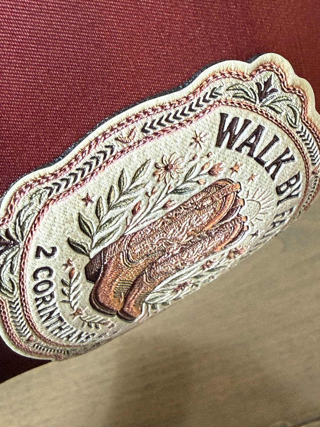 Moss & Maple Signs and Designs embroidered patch on a burgundy trucker hat featuring cowboy boots and floral details.