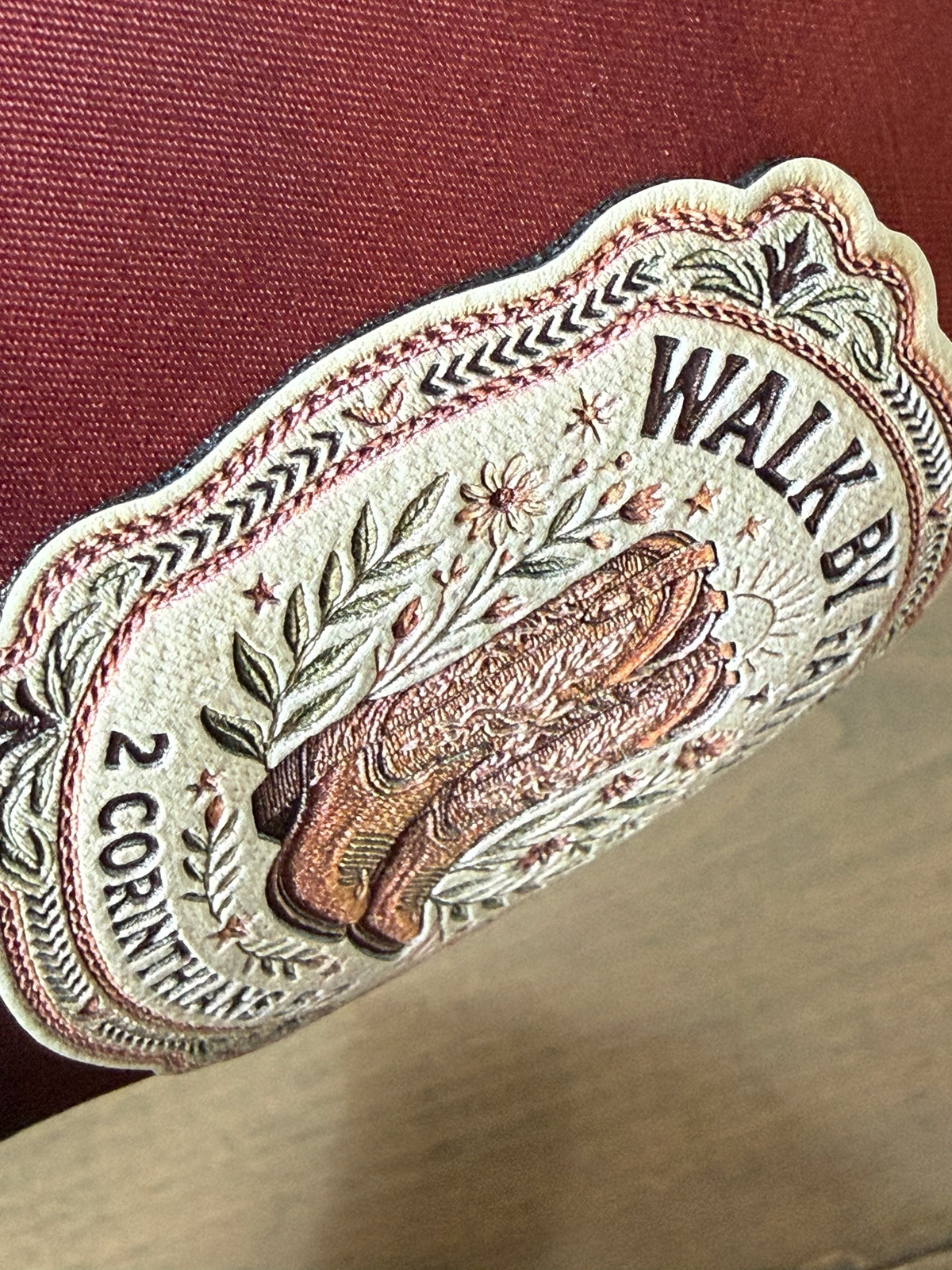 Moss & Maple Signs and Designs embroidered patch on a burgundy trucker hat featuring cowboy boots and floral details.