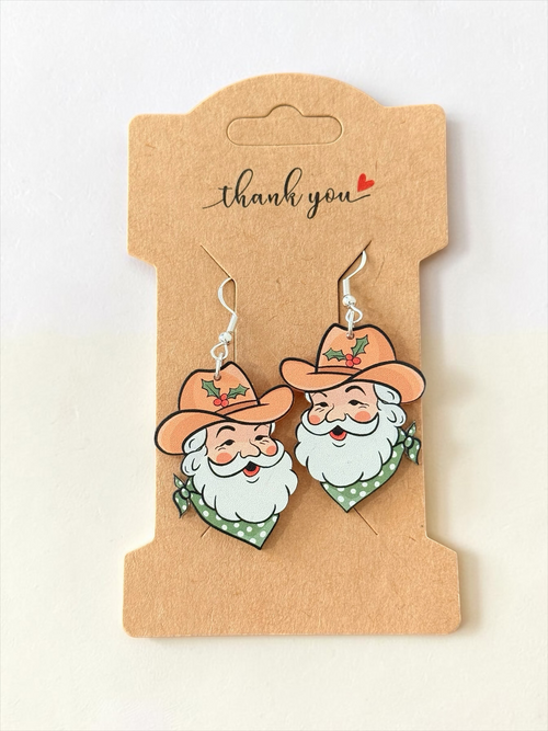 Moss & Maple Signs and Designs Cowboy Santa dangle earrings with tan hats and green polka-dot bandanas on display card